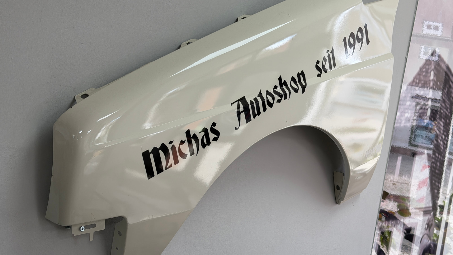 Kotflügel mit Aufschrift „Michas Autoshop seit 1991“ an der Wand